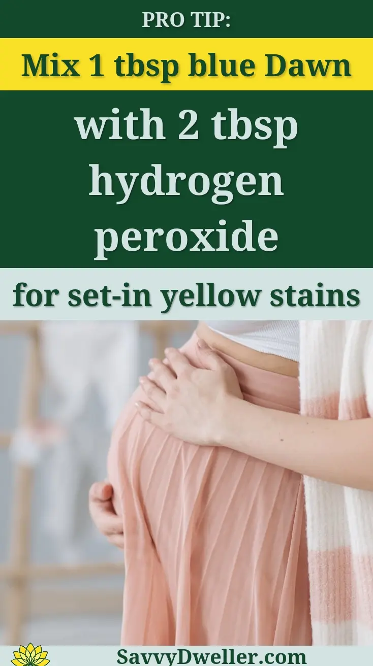 Side view of a pregnant woman indoors, gently holding her belly, wearing a white top and pink skirt.