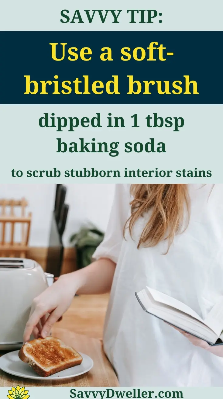 A person using a soft-bristled brush with baking soda to clean the interior of a toaster.