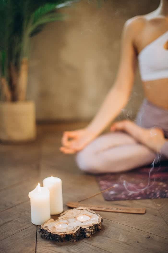 services-04 Woman practicing meditation in lotus pose with candles and incense, focusing on wellness and relaxation.