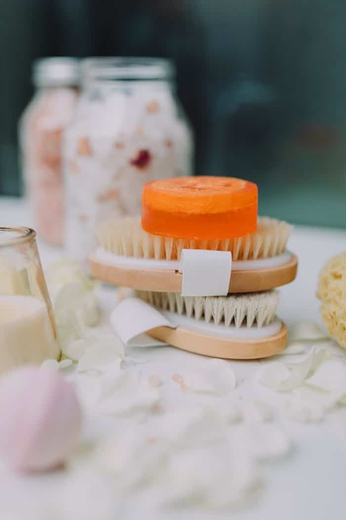 impact-img A stylish arrangement of a natural bath set featuring orange soap, brushes, and bath salts.
